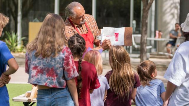 Youth watch a teaching artist explains the printing process