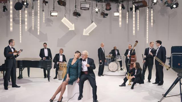 white room with people in suits and dresses standing around looking at each other