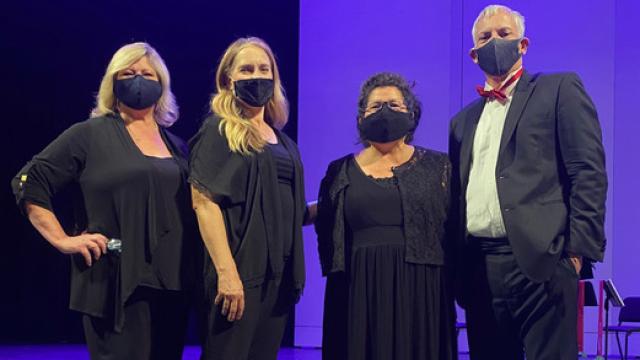 Four musicians, dressed in formal wear and masks, pose in front of a purple backdrop.