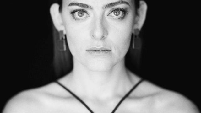Grace Rolland looks into the camera while standing in front of a black background.