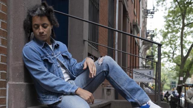 man with dreads sitting on a cement wall looking down