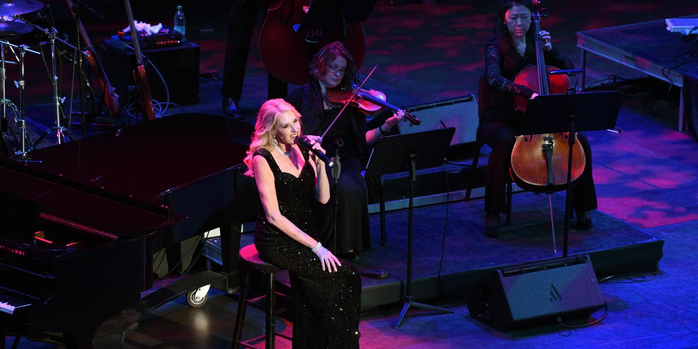 one blonde singer performing while seated on stage. orchestra performs behind her.