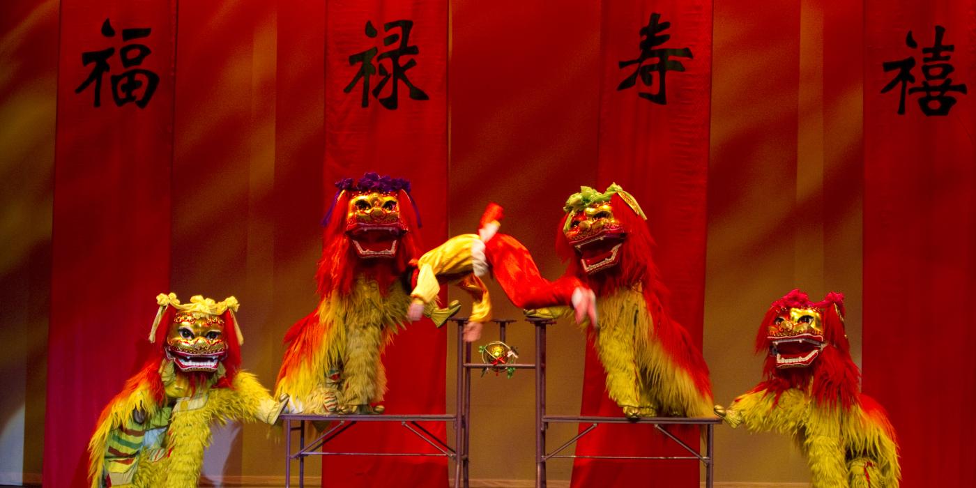 Four colorful red and green Chinese Dragons on stage with a tumbling acrobat