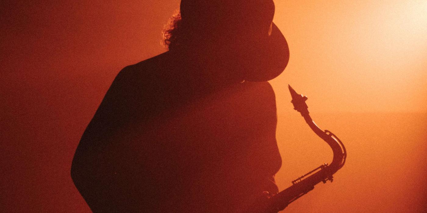 boney james plays his saxophone in a smoky room with red light