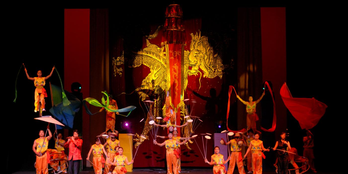 The Peking Acrobats on stage with colorful red and yellow costumes spinning plates