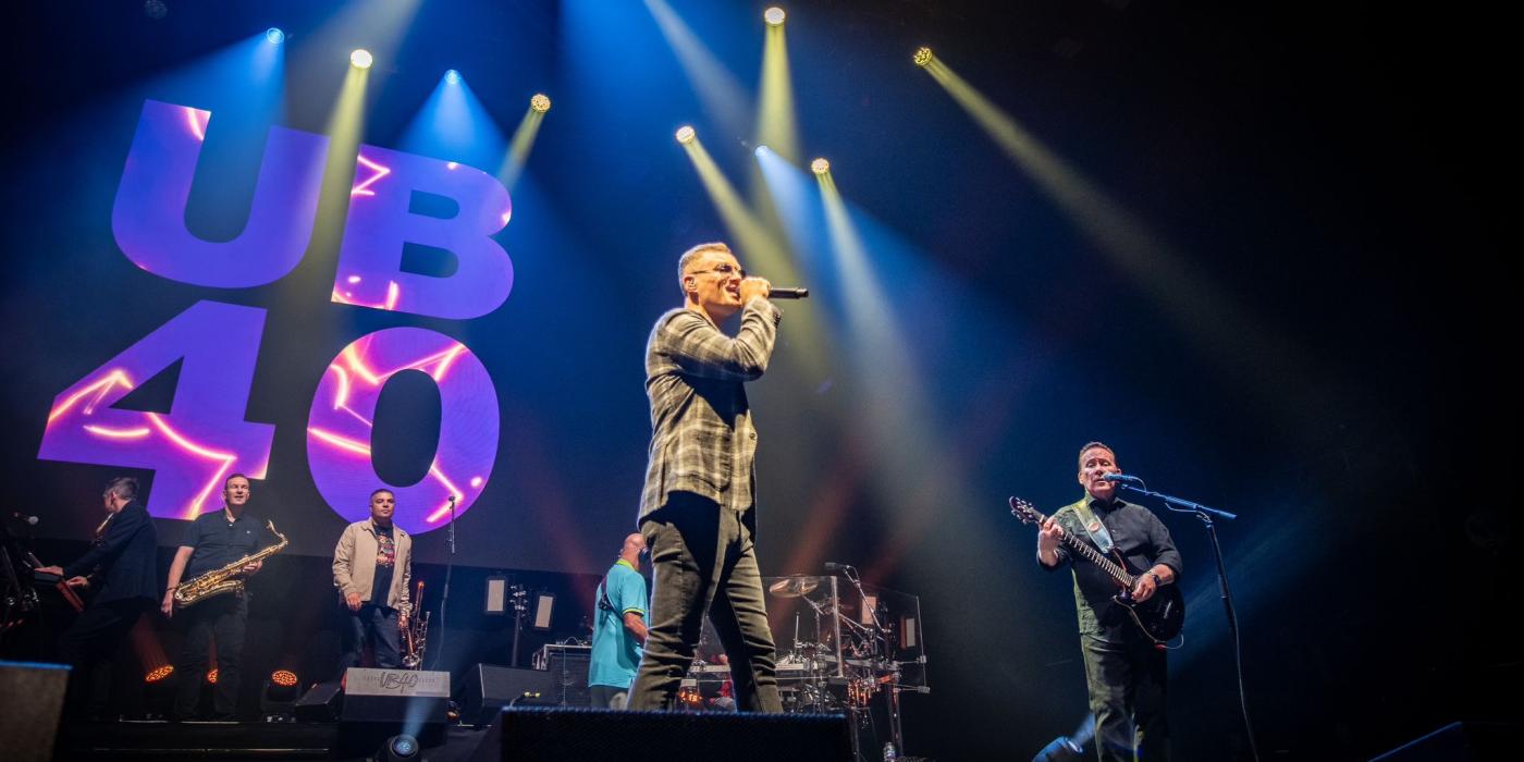 band on stage with UB40 graphic lit up in purple on screen