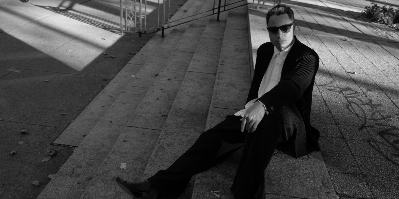 Black and white photo of a male wearing sunglasses, sitting on cement steps.