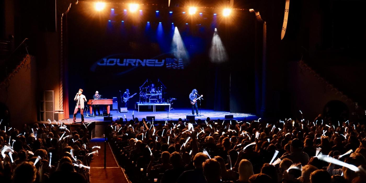 Show attendees with glowsticks and Journey tribute band on stage