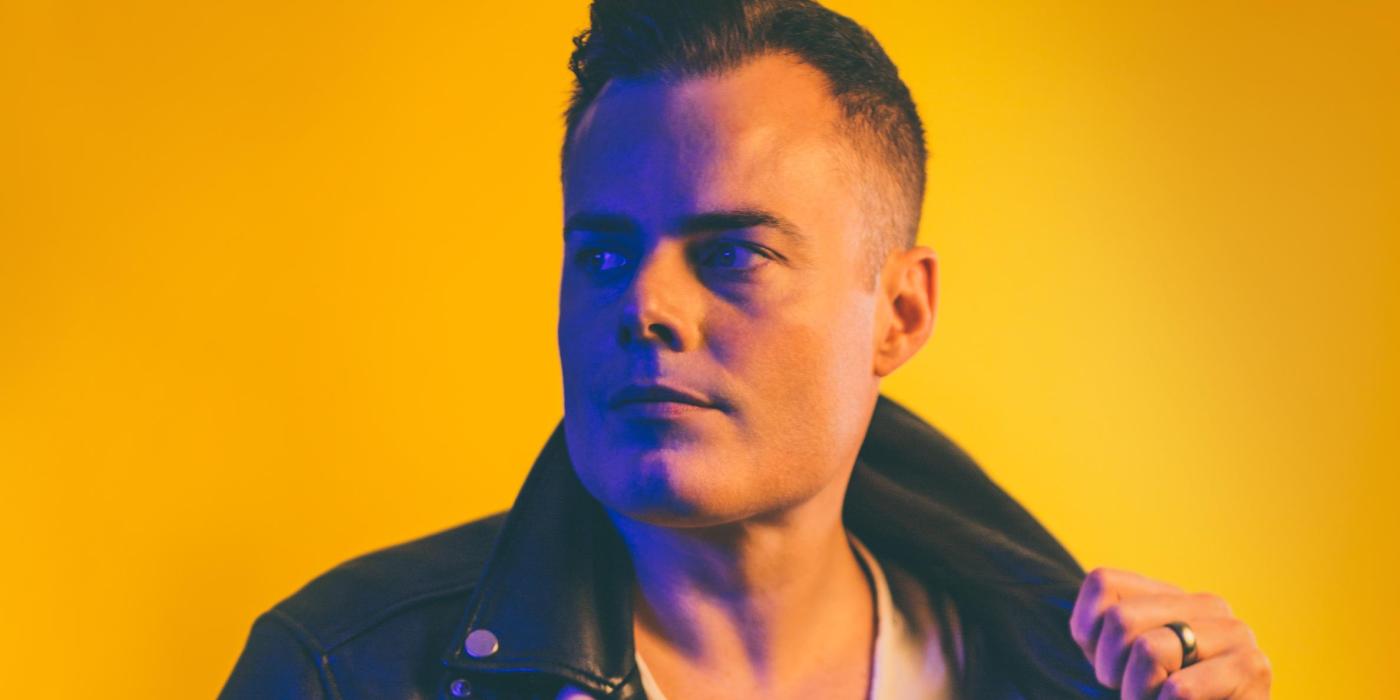 Caucasian male wearing a black leather jacket with a white under-shirt. 