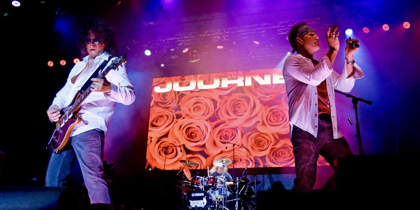 Guitarist and vocalist in foreground, drummer in background on stage
