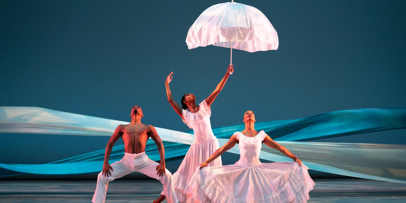 three dancers dressed in white while the dancer in the middle holds a umbrella 
