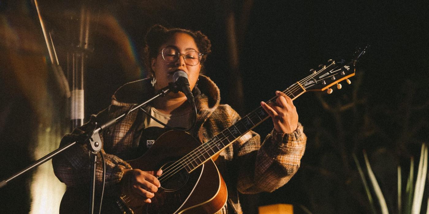 Person playing acoustic guitar and singing into a mic in an outdoor setting
