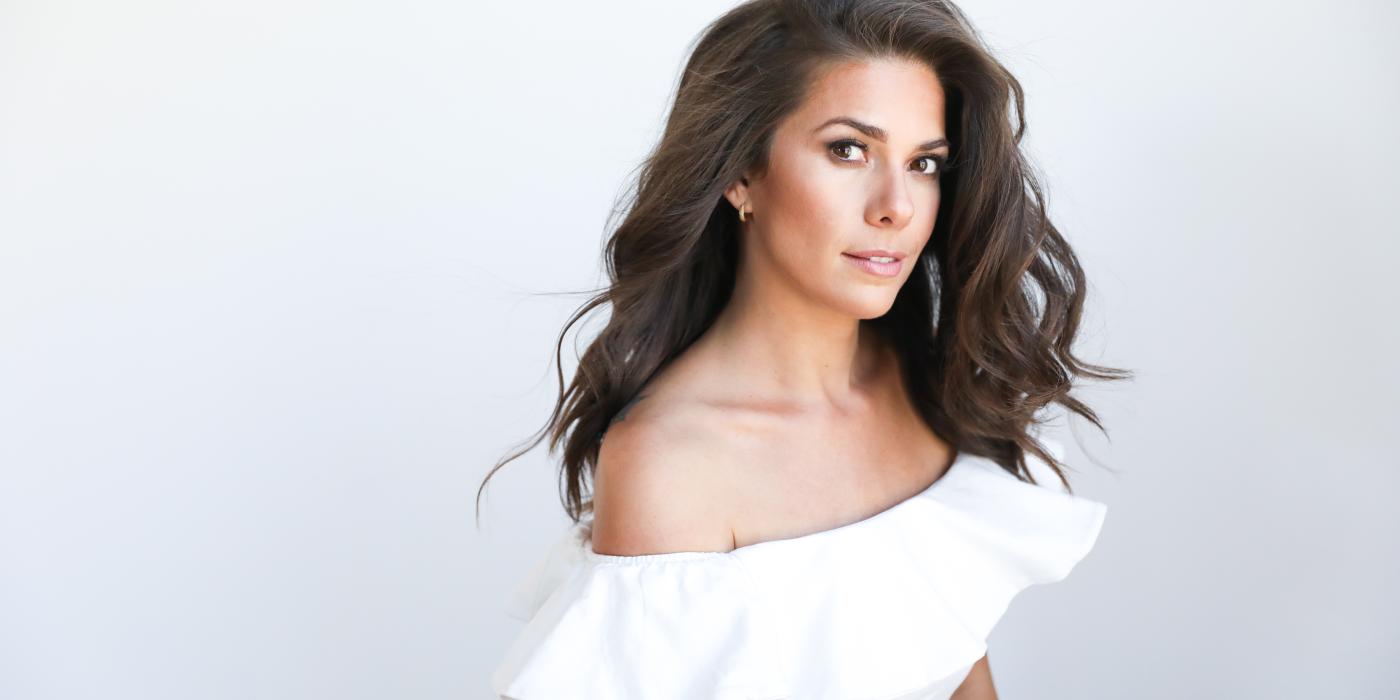 Caro Pierotto dressed in a white dress, her brown hair flowing over one shoulder