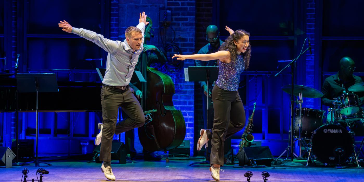 two dancers on stage with both arms outstretched behind them and left legs kicked up behind them