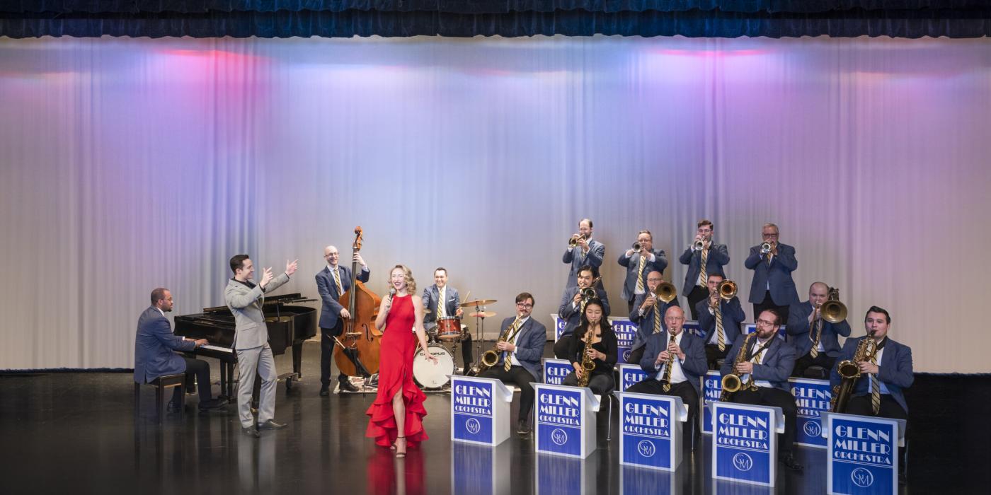 Man and woman singing in front of orchestra on stage
