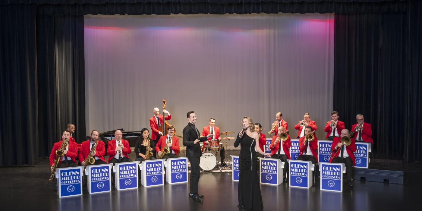 Man and woman singing in front of seated orchestra