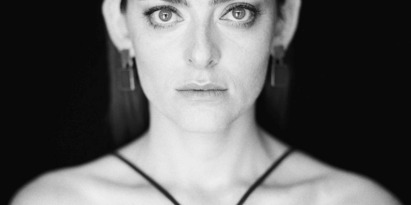 Grace Rolland looks into the camera while standing in front of a black background.