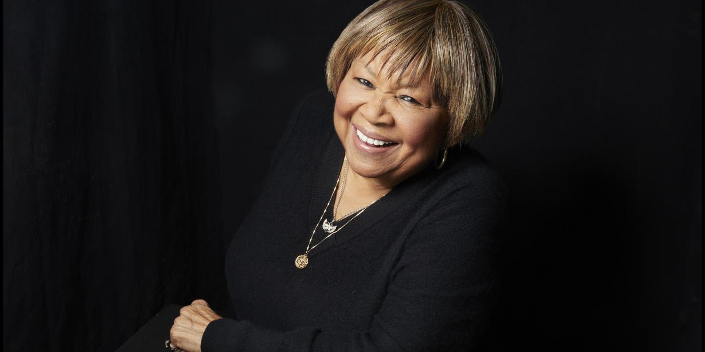Mavis headshot with her smiling at the camera leaning on one arm and dressed in black
