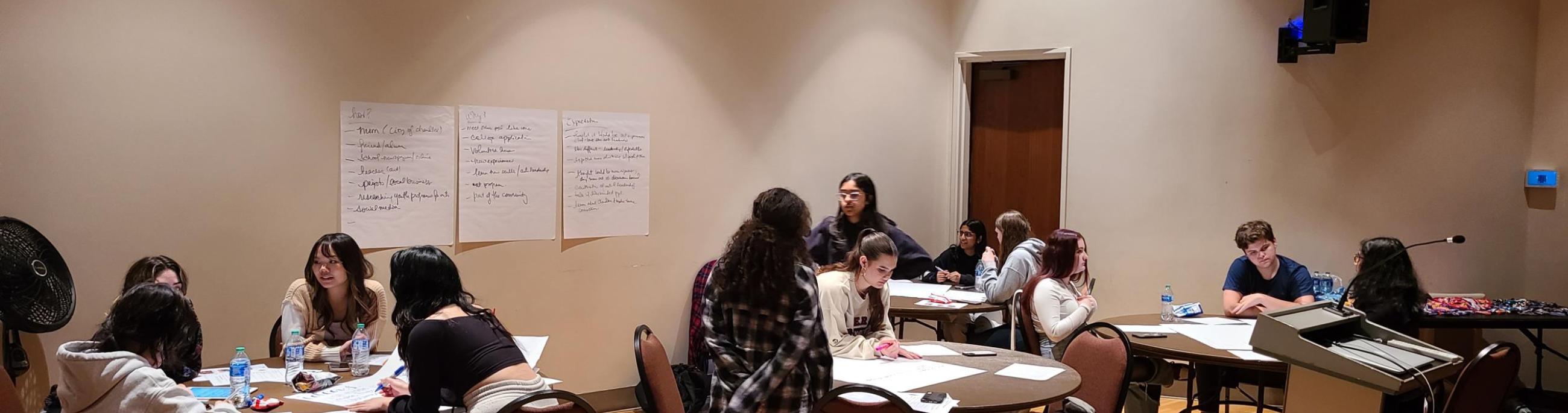 Students work around tables, talking and making notes about a project
