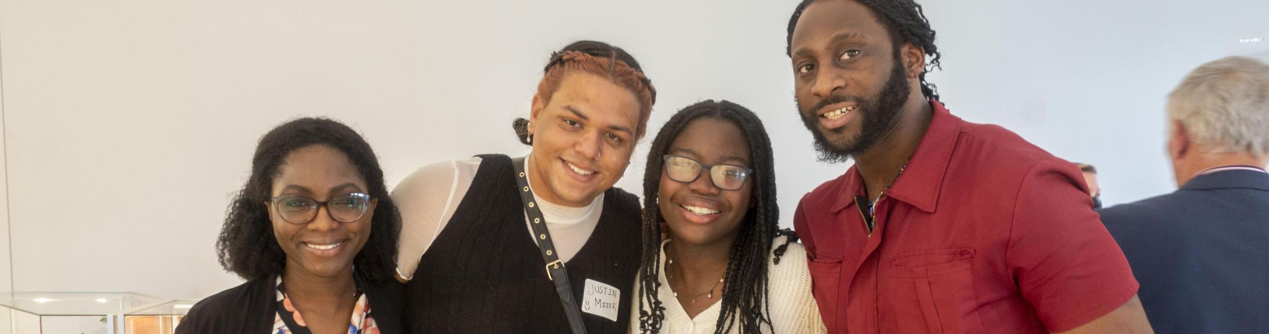 Four people pose, arm in arm, smiling at the camera