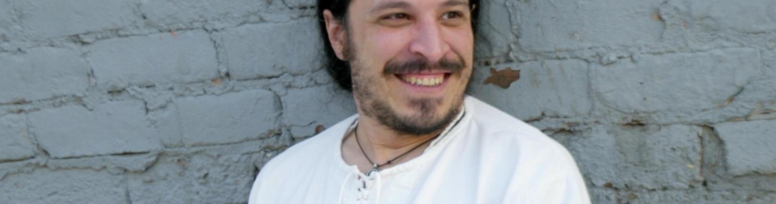 Leon Santiago, wearing a white shirt and white pants, leans back against a white brick wall.
