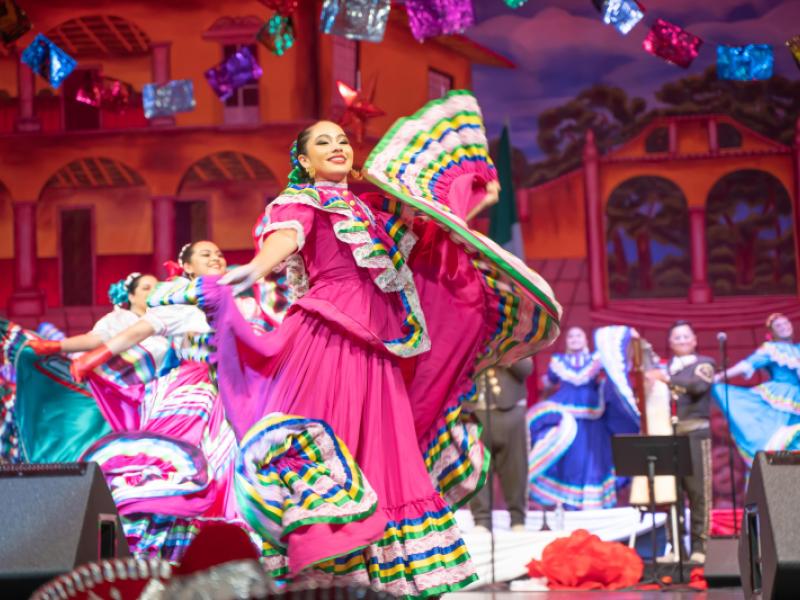 A folklorico dancer in a bright pink dress dances with her skirts fluttering around her