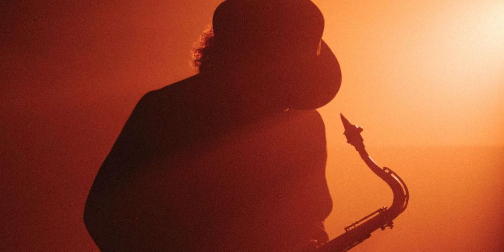 boney james plays his saxophone in a smoky room with red light