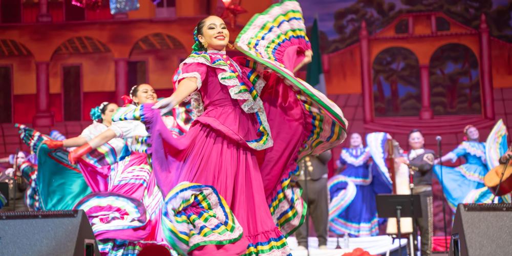 A folklorico dancer in a bright pink dress dances with her skirts fluttering around her