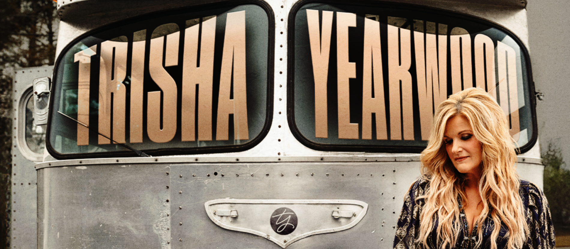 Blonde woman standing in front of silver bus that says Trisha Yearwood