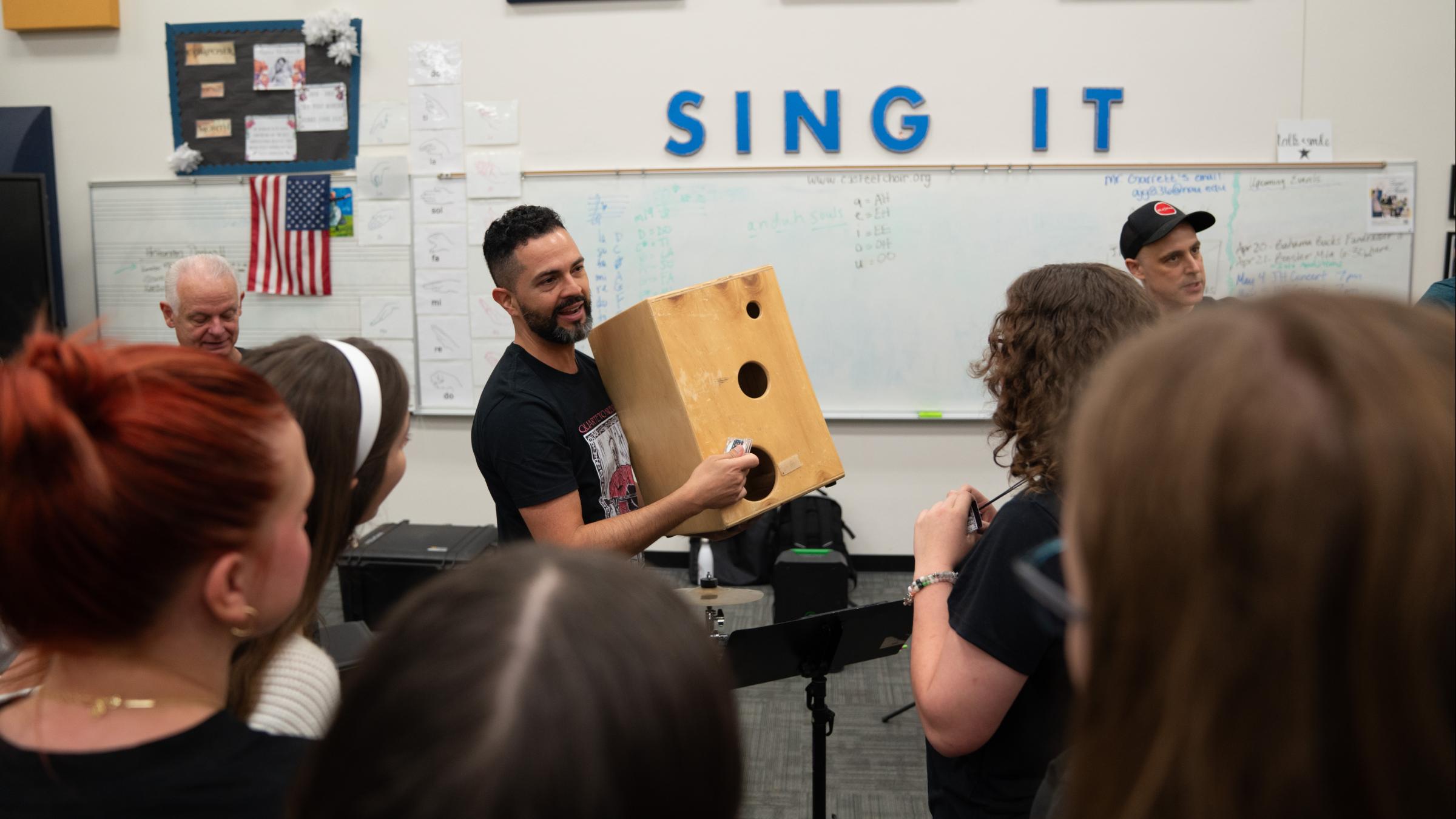 percussionist shows a group of students how to play a cajon